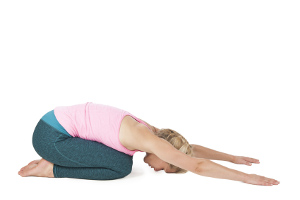 Yoga-Serien-Bild: seitliche Ganzkörper-Profil-ansicht einer blonden Frau mittleren Alters die Yoga-Übung Hund (Adho Mukha Svanasana) zeigend; Position 9:  Yoga-Stellung des Kindes (Garbhasana) mit nach vorn ausgestreckten Armen vor weißen Hintergrund