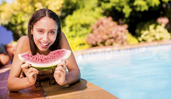 Woman at the edge of a swimming pool eating watermelon