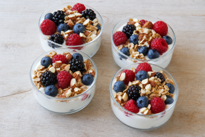 Vier Glasschalen mit Skyr-Magerquark-Creme, Beeren und gerösteten Haferflocken mit Mandeln.