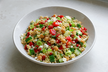 Couscous-Salat mit Kichererbsen, Gojibeeren, Paprika, Gurke und frischen Kräutern in einer Schüssel.