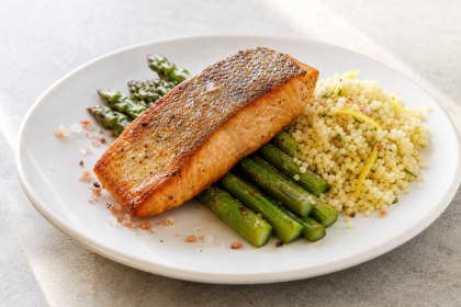 Gebratener Lachs mit grünem Spargel, Zitronen-Couscous und rotem Hawaii-Salz auf einem Teller