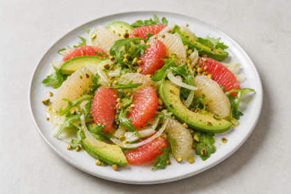 Pomelo-Grapefruit-Salat mit Avocado, Fenchel, Rucola und Pistazien auf einem hellen Teller.