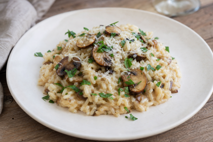 Cremiges Risotto mit gebratenen Champignons, geriebenem Hartkäse und Petersilie auf einem Teller.