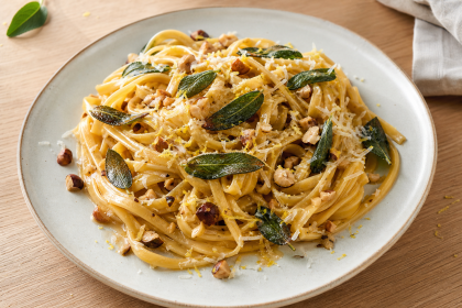 Tagliatelle mit Salbeibutter, gerösteten Haselnüssen, Parmesan und Zitronenabrieb auf einem hellen Teller.