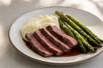 Wagyu-Steak in Scheiben mit Kartoffelstampf, grünem Spargel und Schalottenjus auf einem Teller