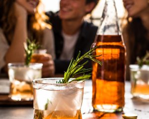Alkoholfreier Rhabarber-Spritz vor einer Gruppe junger Menschen; vom VdF KI-bearbeitetes Pressebild