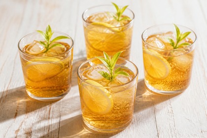 Vier Gläser bernsteinfarbene Colakraut-Limonade mit Zitronenscheiben