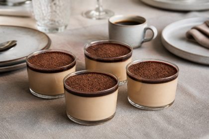 Vier Gläser Espresso-Panna-cotta mit Espressosirup und Kakaopulver