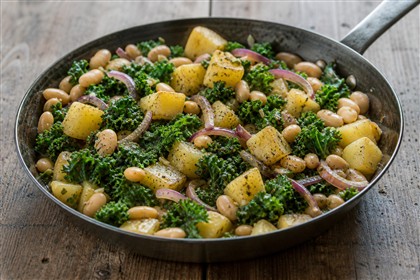 Pfannengericht mit Grünkohl, Kartoffelwürfeln, weißen Bohnen und roten Zwiebeln