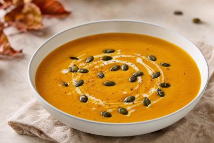 Orangefarbene Hokkaido-Kürbissuppe mit Sahnespur und gerösteten geschälten Kürbiskernen in einer hellen Schale