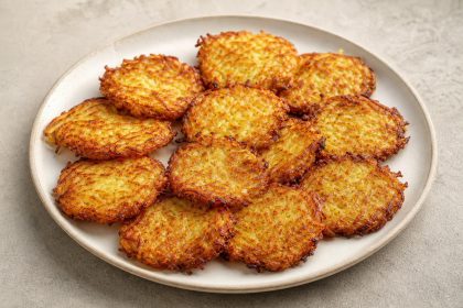 Goldbraun gebackene Kartoffelrösti mit knusprigen Rändern auf einer hellen Keramikplatte.