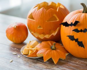 Geschnitzte Halloweenkürbisse, Kürbisstücke und Kerne auf einem Holztisch.