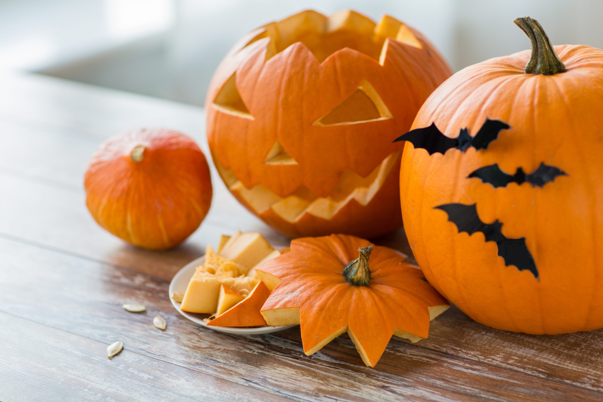 Geschnitzte Halloweenkürbisse, Kürbisstücke und Kerne auf einem Holztisch.