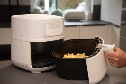 Weiße Heißluftfritteuse mit herausgezogenem Garkorb und Pommes auf einer Küchenarbeitsplatte.