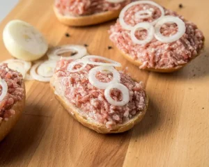 Mettbrötchen mit rohen Zwiebelringen auf einem Holzbrett.
