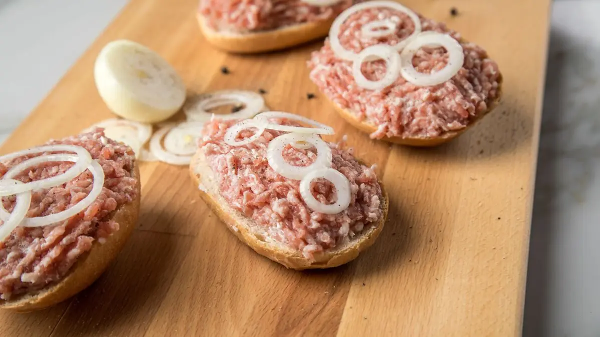 Mettbrötchen mit rohen Zwiebelringen auf einem Holzbrett.