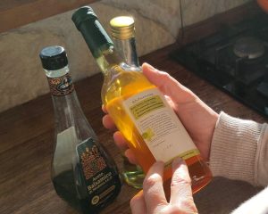 Hände halten eine Essigflasche vor weiteren Flaschen auf einer Küchenarbeitsplatte