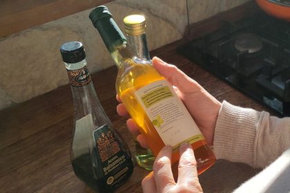 Hände halten eine Essigflasche vor weiteren Flaschen auf einer Küchenarbeitsplatte